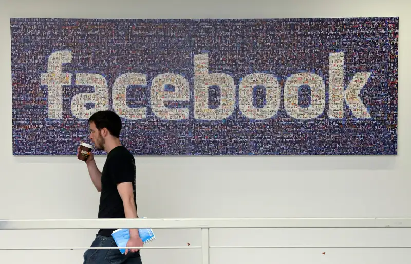 In this March 15, 2013, file photo, a Facebook employee walks past a sign at Facebook headquarters in Menlo Park, Calif.