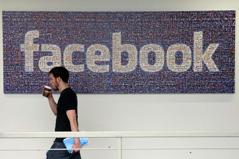 In this March 15, 2013, file photo, a Facebook employee walks past a sign at Facebook headquarters in Menlo Park, Calif.