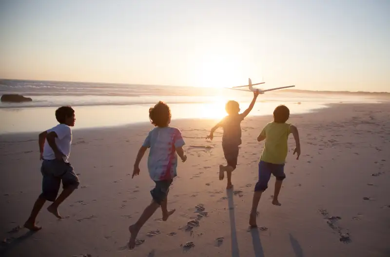 Boys running along beach with a toy plane