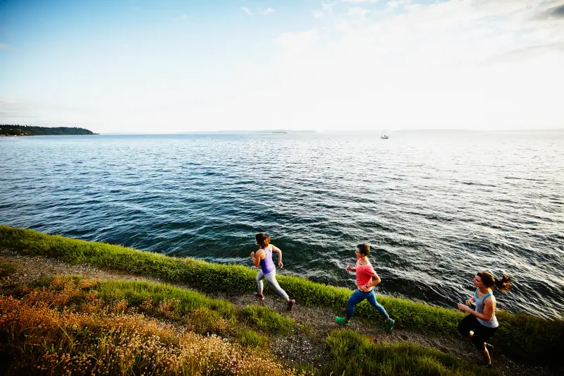 Three women running together on path at sunset