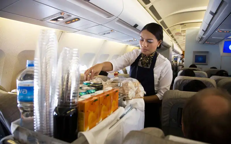 B79MG3 Cabin crew / air stewardess serves drinks to passengers from a trolley cart during a flight (45)