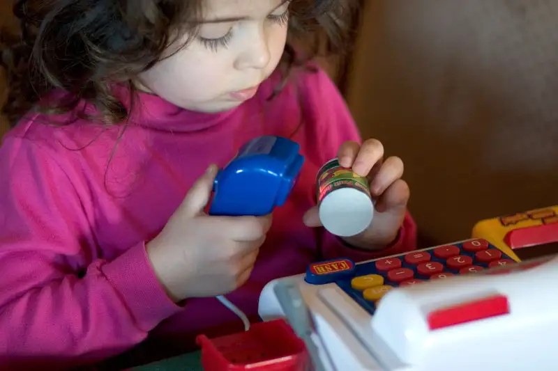 Girl age 3 scanning item at toy cash register. Plainfield Illinois IL USA