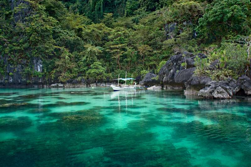An outrigger canoe hidden in a lagoon among the islands of El Nido, enabling tourists on board to take a bath in the turquoise waters of Palawan archipelago.