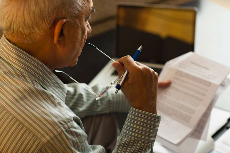 Senior man reading document near laptop on coffee table
