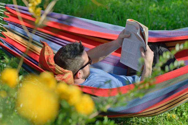 Germany, Young man lying in hammock and reading a magazine