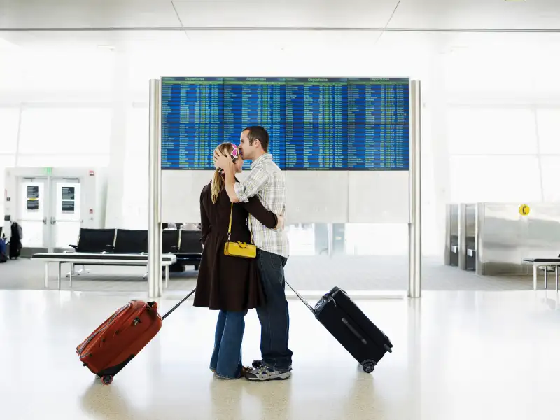 Man kissing woman in airport near departure board