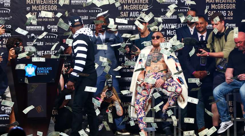 Floyd Mayweather Jr. looks on as money rains down on Conor McGregor during a press event promoting their boxing match on Saturday, August 26.