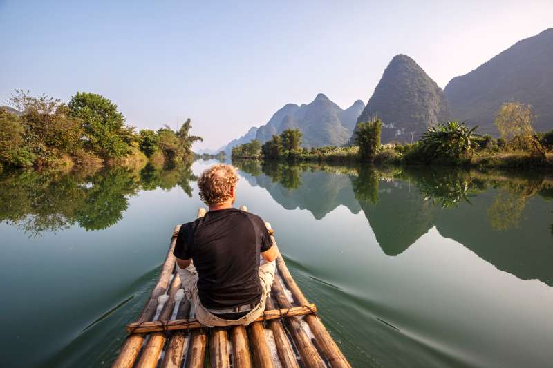 China, Guanxi, Yangshuo, Tourist on bamboo boat on the Li river looking at famous karst peaks
