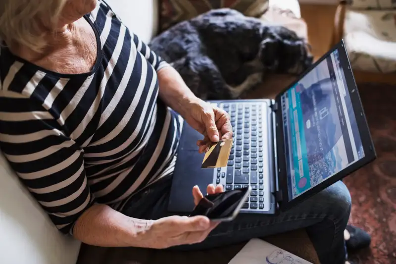 High angle view of senior woman with technologies and credit card sitting by dog on sofa