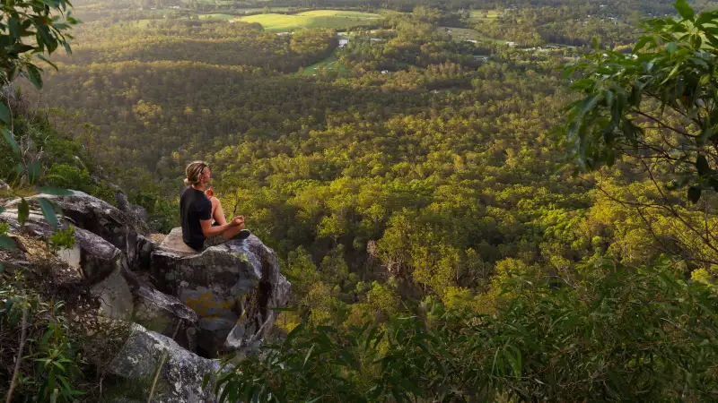 A young man meditates on top of a mountain with expansive views near Noosa Heads, Australia.