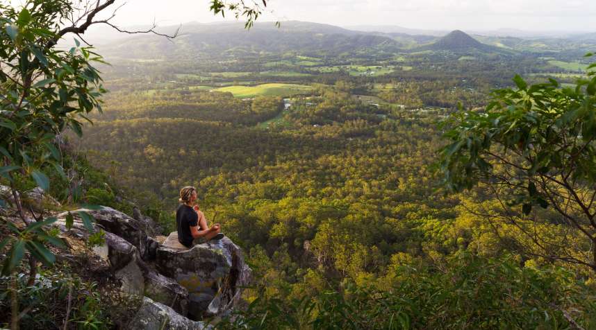 A young man meditates on top of a mountain with expansive views near Noosa Heads, Australia.