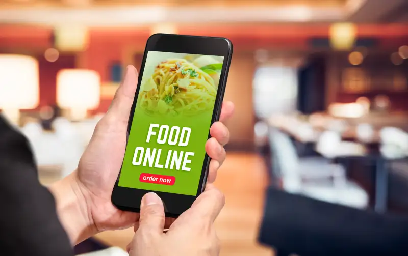 Close up hand holding mobile phone with order food online word on screen with blur restaurant bokeh light background,online food marketing concept.