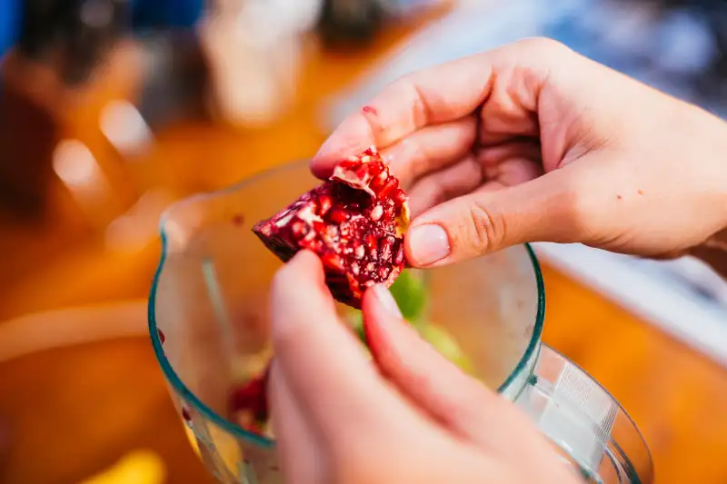 Caucasian woman making smoothie in a blender using pomegranate.
