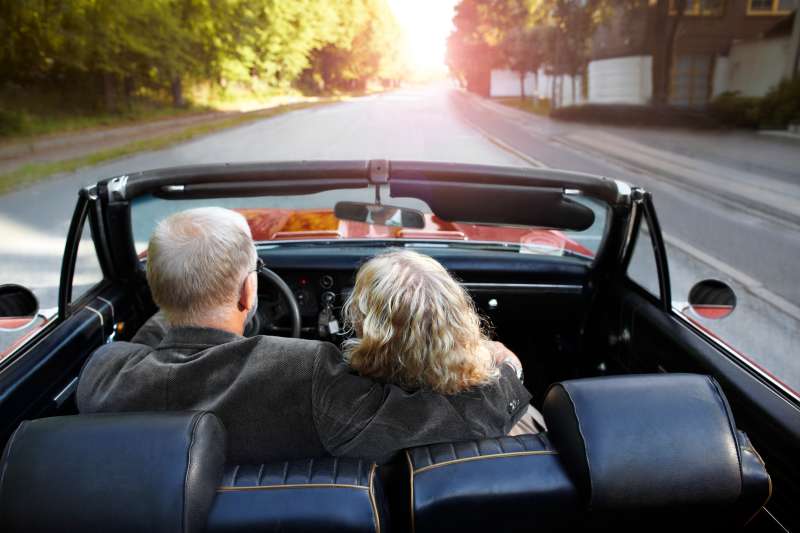 Mature couple driving convertible car in sunset