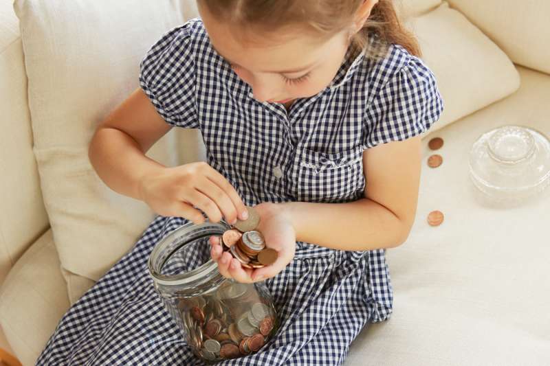 Young girl, sitting on sofa, counting money from jar, elevated view