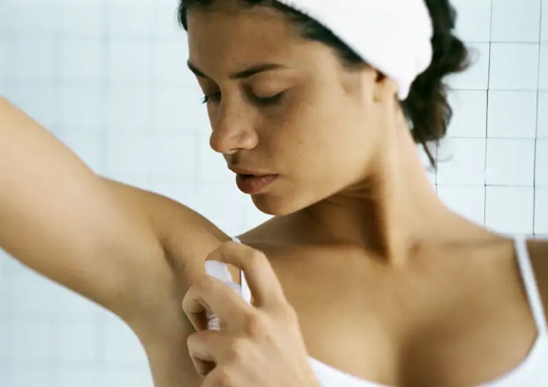 Young woman spraying underarm, head and shoulders