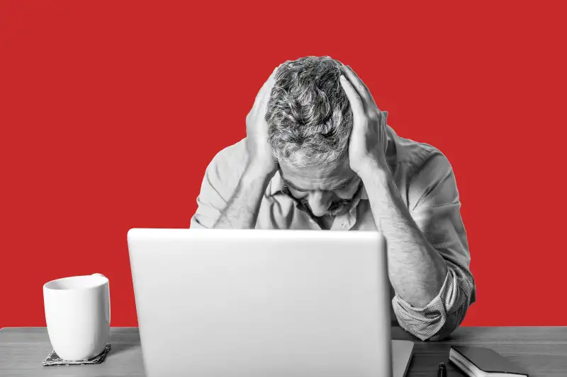 Angry businessman with head in his hands sitting at his home office