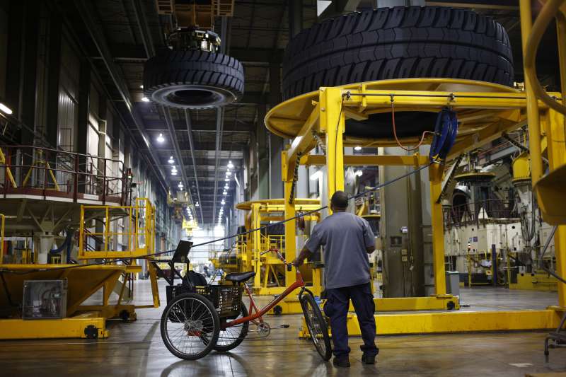 An employee watches as a newly-manufactured Michelin &amp; Cie. earthmover tire is suspended above the factory floor