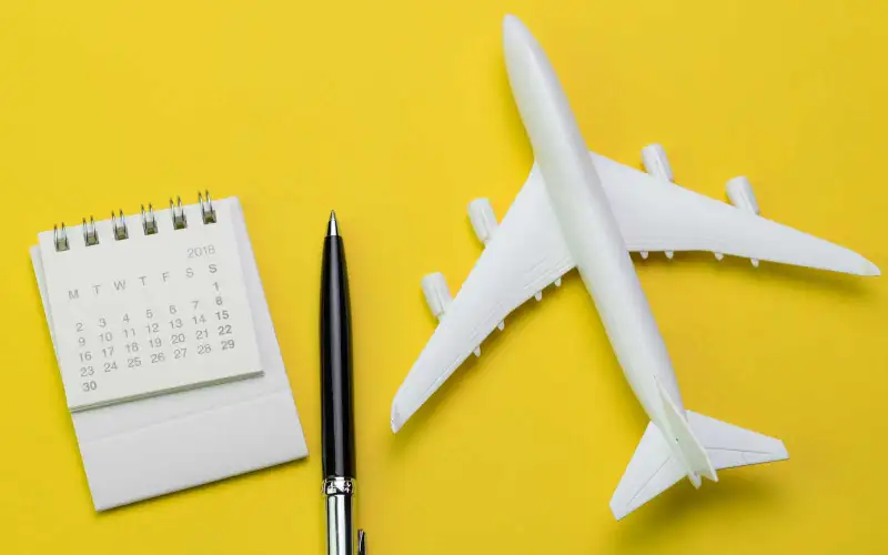 Flat lay of travel and tourism concept, small white clean paper calendar with black pen and toy airplane on vibrant yellow background