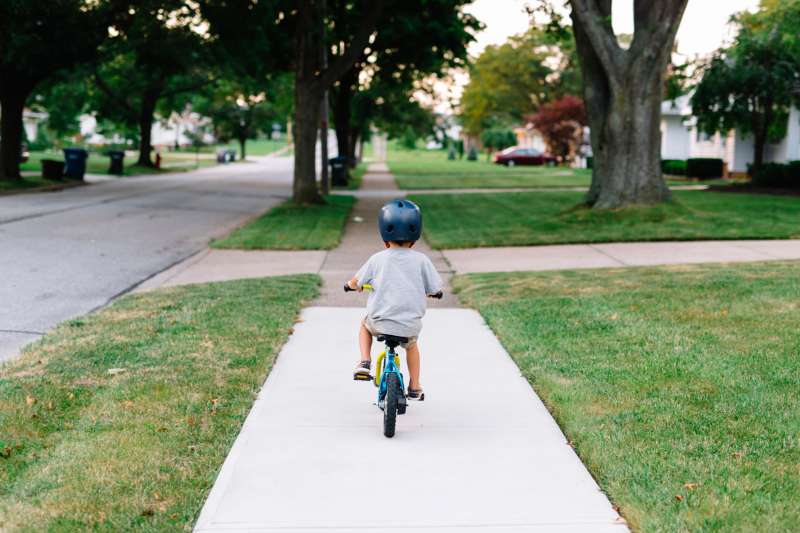 Rear view of young boy wearing crash helmet cycling along a pavement.