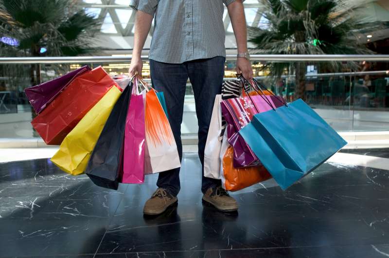 Man holding shopping bags in mall, low section