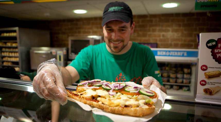 A Subway employee preparing a footlong sandwich.