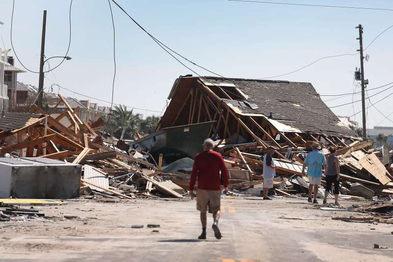 People walk along a street blocked by a building  after Hurricane Michael passed through the area on October 11, 2018 in Mexico Beach, Florida.  The hurricane hit the panhandle area with category 4 winds causing major damage.