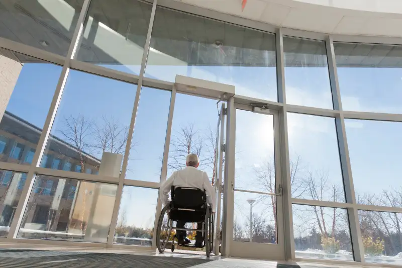 Doctor with muscular dystrophy in wheelchair leaving hospital entrance