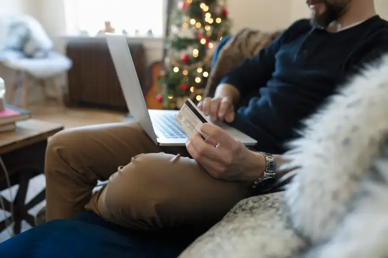Young man with credit card online Christmas shopping on laptop