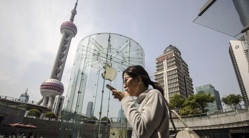 A woman using a smartphone walks past an Apple Inc. store in Shanghai.