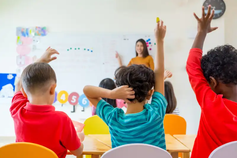 Rear View Of Students Sitting With Teacher