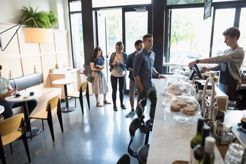 Male worker helping customers in queue at cafe counter