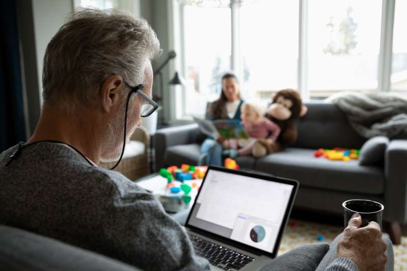 Senior man using laptop and drinking coffee in living room