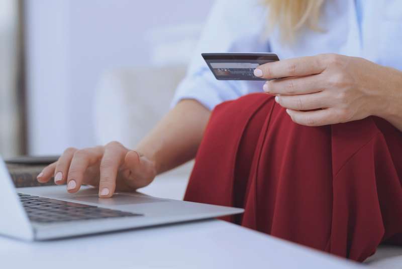 Blond woman sitting on couch, using laptop to make a payment with her credit card