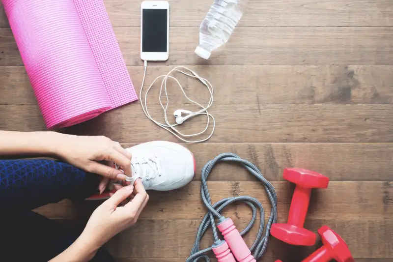 Low Section Of Woman Tying Shoe While Kneeling On Hardwood Floor