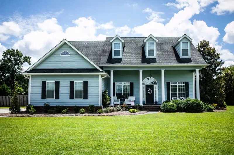 pale blue house with siding on a large lot with traditional windows and shutters in a subdivision in the suburbs on a bright sunny blue sky day