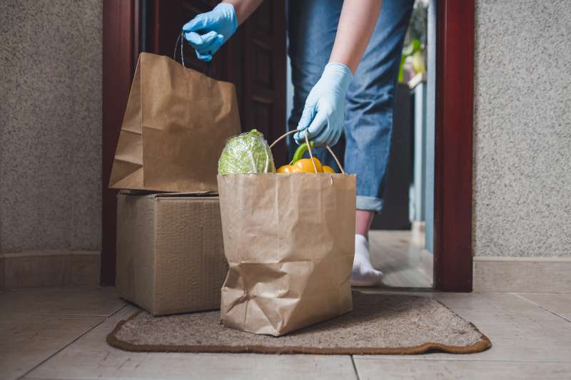 person's gloved hands picking up groceries in brown bags