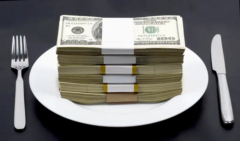 Stack of wrapped bills on top of a dinner plate with a fork and a knife on either side