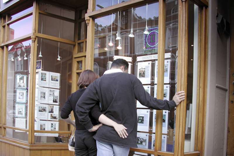 A couple looking at the listings in the real estate office window.