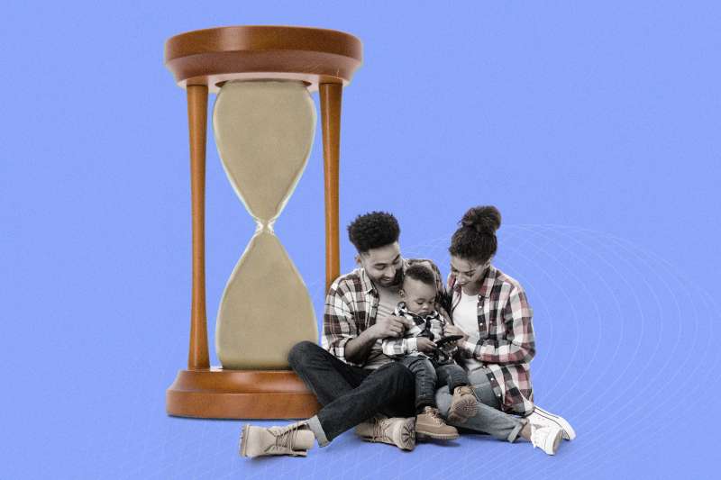Mother and Father with 1 year old son sitting in front of an oversized hourglass that is completely full of sand