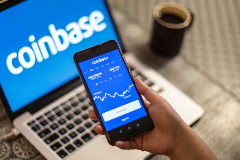 Coinbase logo is seen displayed on a smartphone and a laptop in the background