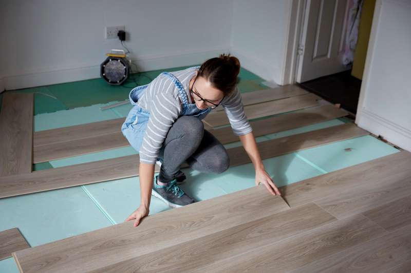 Woman laying new floorboards in the living room of a house under renovation