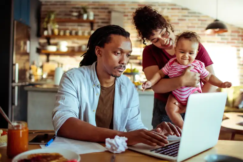 Young couple looking at something on a laptop with a new born baby