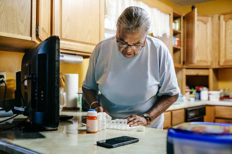 Senior black woman standing in kitchen sorting her medication for the week.