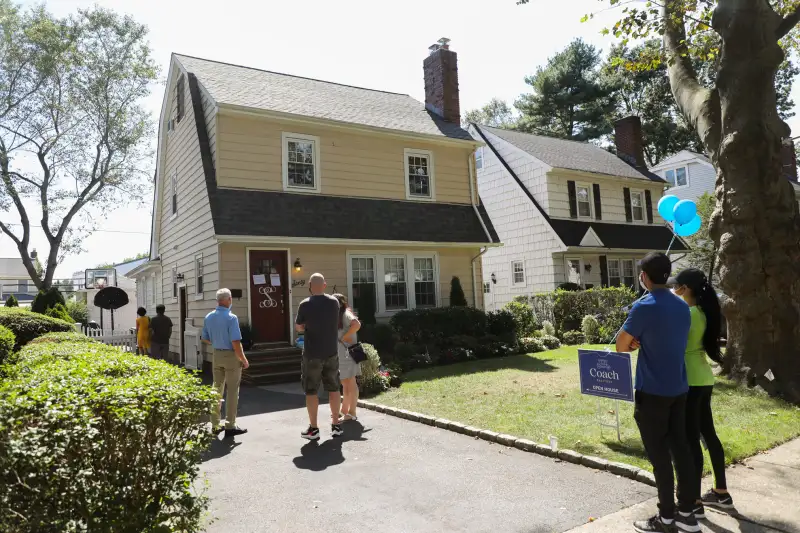 People wait outside in a line to visit a open house in the suburbs