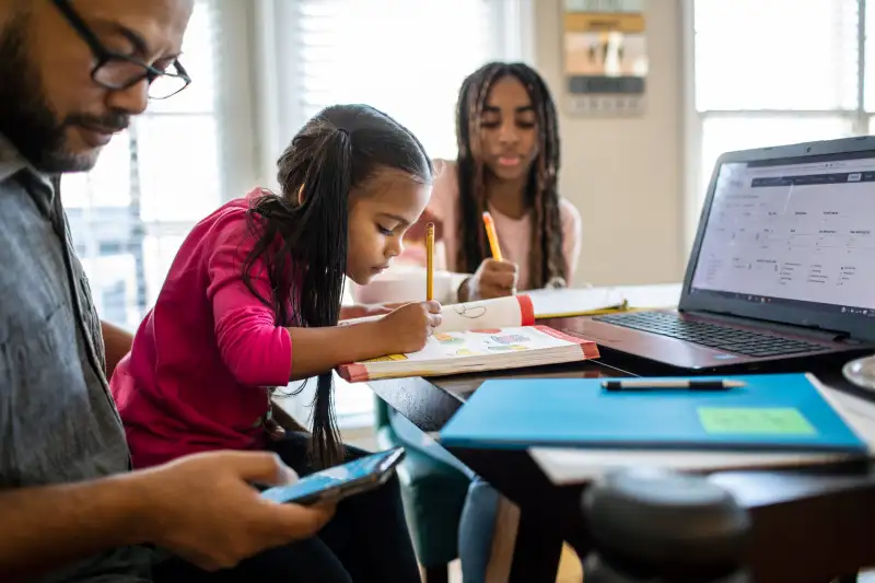 Father working from home while daughters work on their homework