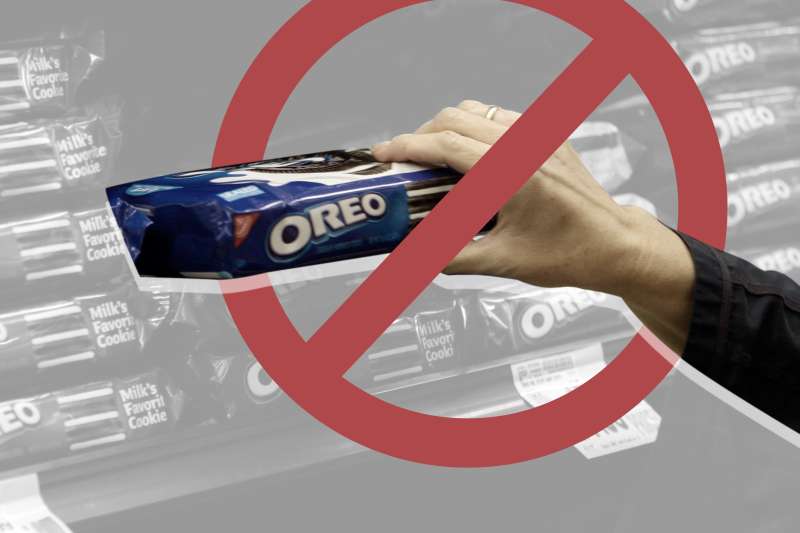 A hand holding a packet of Oreos at the store with a a big cross out signal
