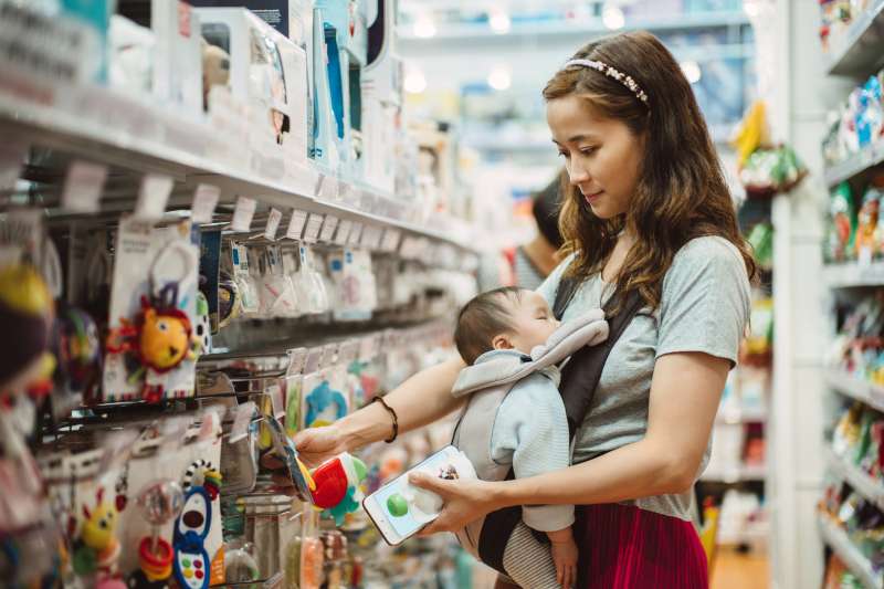 Young mom shopping for baby products while carrying her sleeping baby