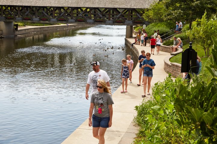 People walk along a river on a sunny day in Naperville Illinois