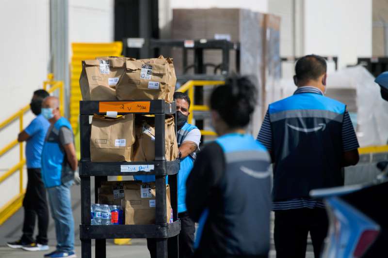 An Amazon.com delivery driver pushes a cart of groceries to load into a vehicle outside of a distribution facility
